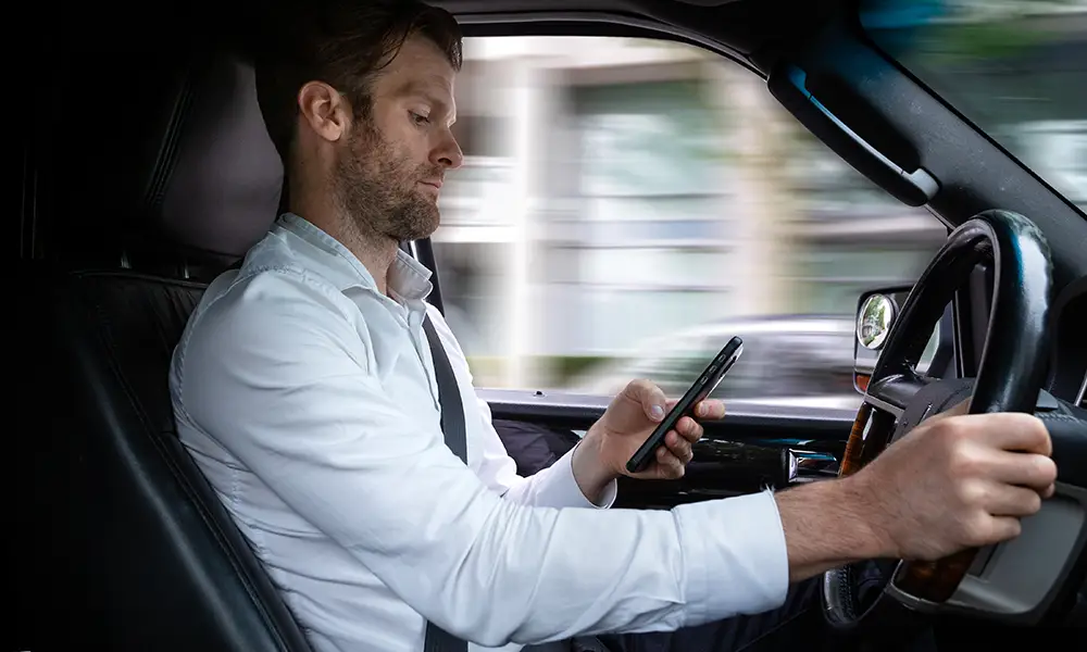 man driving while being distracted by texting on a mobile phone.