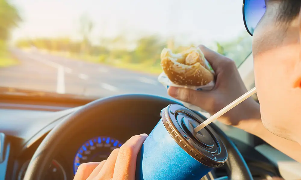 person driving on the road while distracted by eating and drinking.